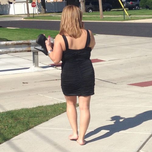 young woman in black dress doing the walk of shame carrying her shoes